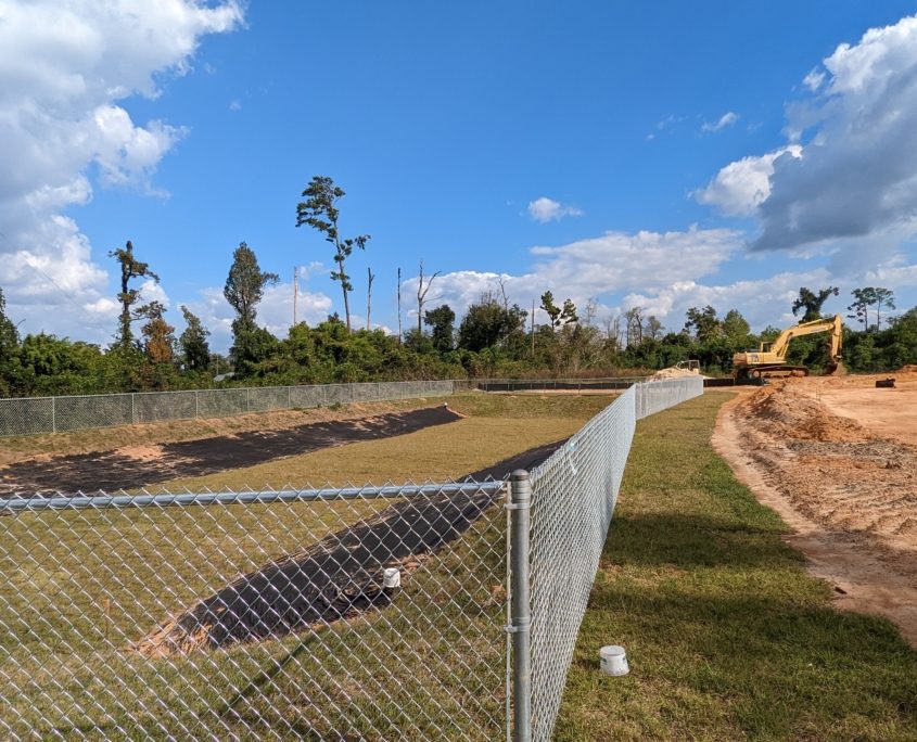 An image showing a chain link fence surrounding an empty water retention pond